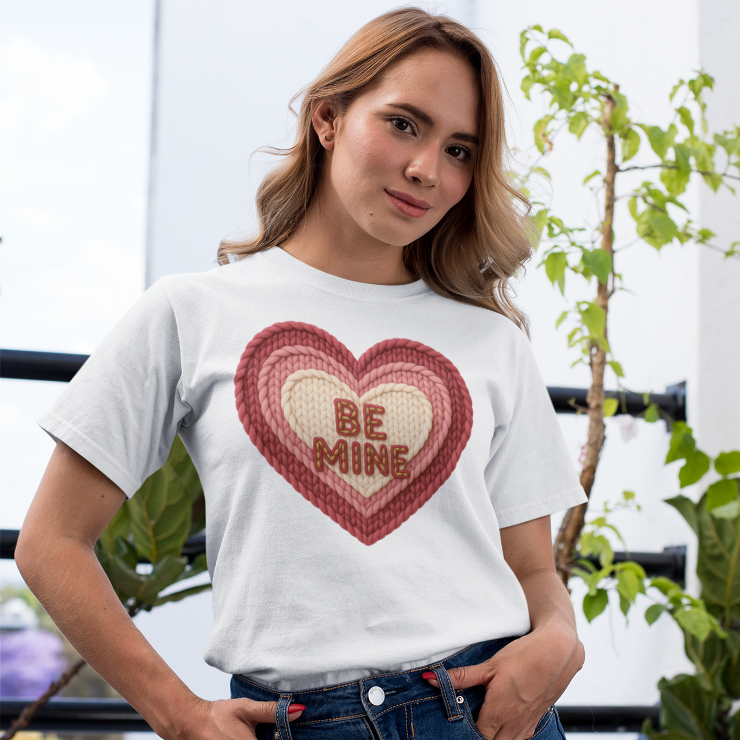 Woman wearing a white t-shirt with a red heart design and 'BE MINE' text, standing outdoors.