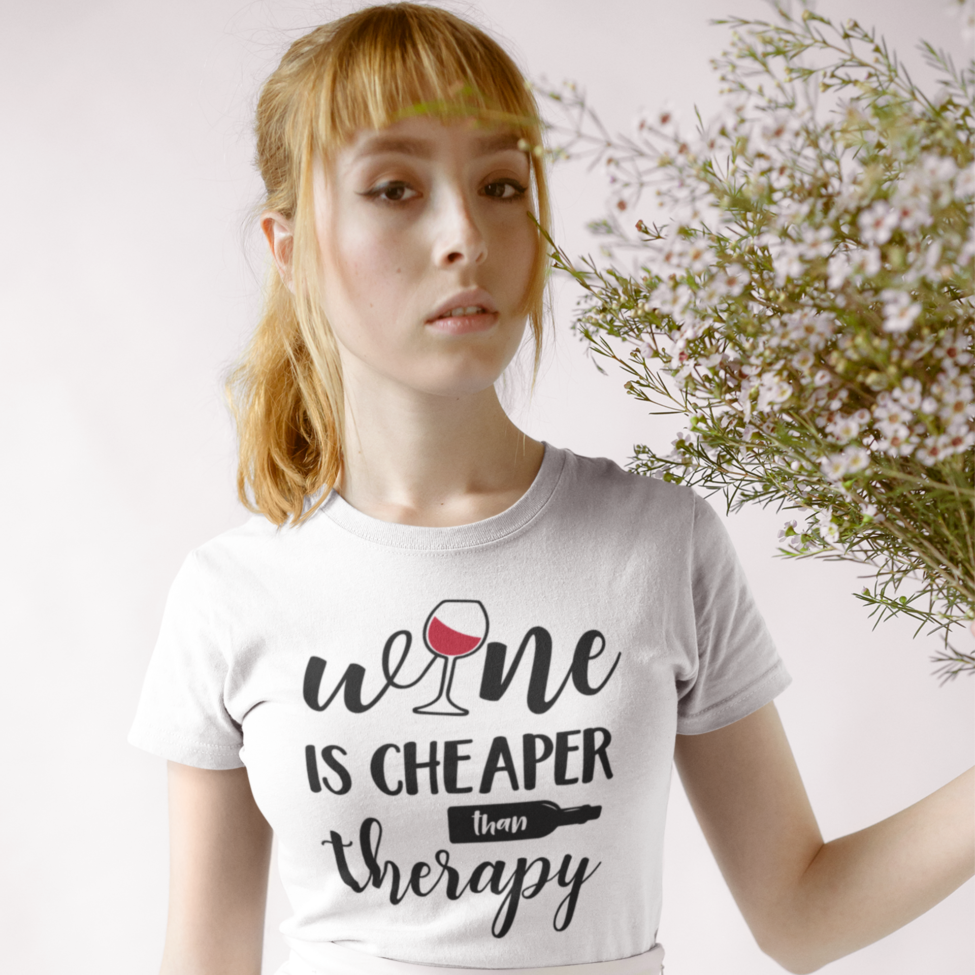 Person wearing a white t-shirt with 'wine is cheaper than therapy' text, holding flowers.